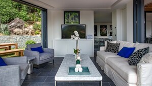 A modern living room with a stone wall, a TV, a coffee table, and a sofa with patterned cushions. - Beautiful Sasha Luxury villa (Corossol)