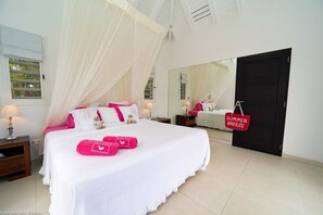 A bedroom with a large bed, white bedding, a canopy, a mirror, and a door with a sign.