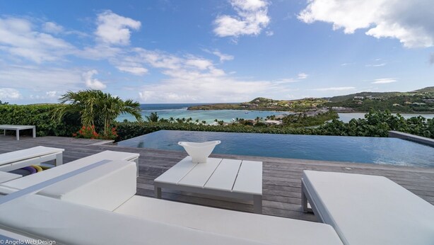 Zona de piscina con sillones blancos y vistas al océano y las colinas.