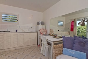 A modern kitchen with white cabinets, a dining area with a table and chairs, a large mirror, and a view of greenery outside.