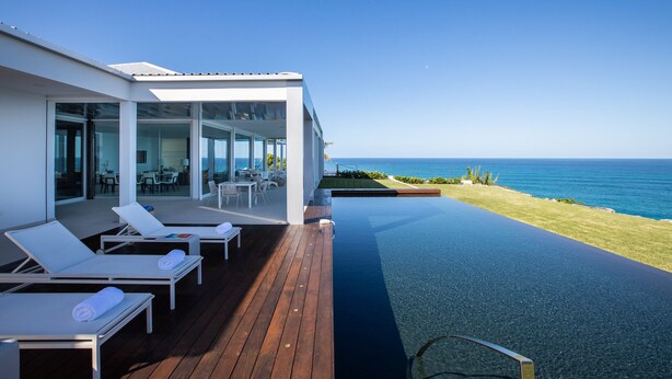 Ett modernt hus med pool, solstolar och utsikt över havet.