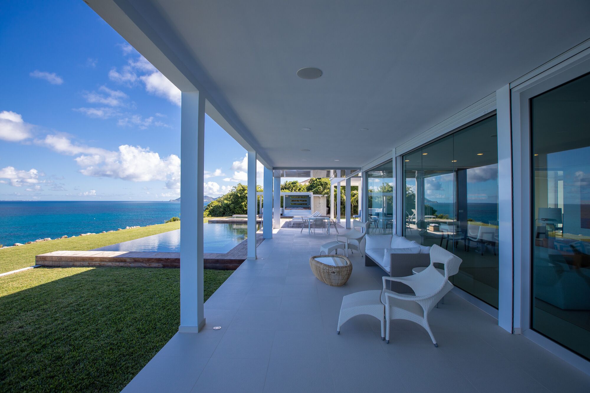 A modern outdoor lounge area with a pool, white furniture, and a view of the ocean.