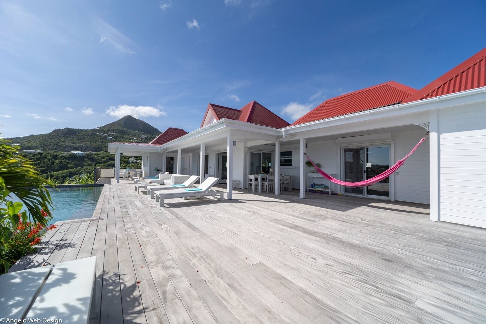 Una terrazza in legno con poltrone relax e un'amaca, con vista su una piscina e un paesaggio montuoso.