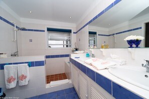 A bathroom with a shower, two sinks, a window, and a mirror.