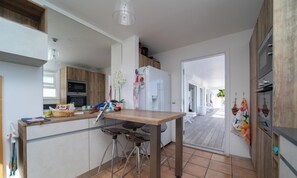 A modern kitchen with a wooden table, bar stools, and a view to a covered outdoor area. - Minou (2/4 Rooms) Luxury villa (Grand Cul de Sac)