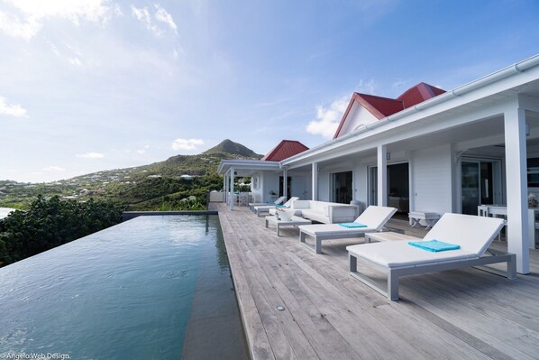 A poolside area with lounge chairs and a wooden deck overlooking a body of water and a hilly landscape.