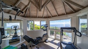 Uma academia com equipamentos de ginástica, amplas janelas e vista para o oceano.
