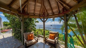 Un espacio de estar techado al aire libre con dos sillas y una mesa, con vista a un paisaje marino.