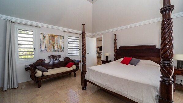 Un dormitorio con cama con dosel, un banco de madera y un ventanal con persianas.