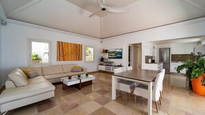 Uma sala de estar moderna com sofá, mesa de centro e mesa de jantar. Há uma cozinha com geladeira e armários.