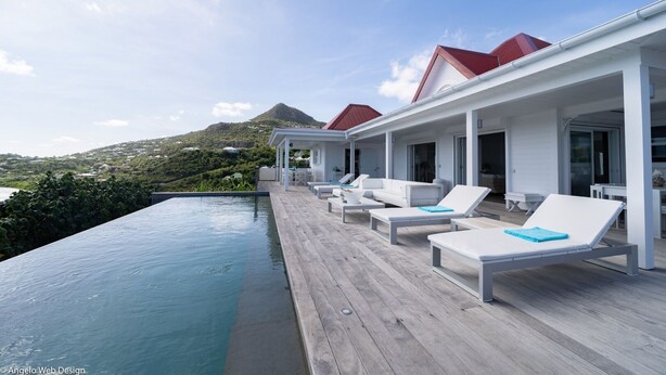 Un espace aménagé au bord de la piscine, avec des chaises longues et une terrasse en bois offrant une vue sur un plan d’eau et un paysage vallonné.