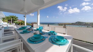 A dining table set for four with turquoise plates and glasses, overlooking a coastal view. - Beautiful Minou Luxury villa (Grand Cul de Sac)