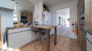 A modern kitchen with a wooden table and bar stools, a refrigerator, and a window overlooking a deck. - Beautiful Minou Luxury villa (Grand Cul de Sac)