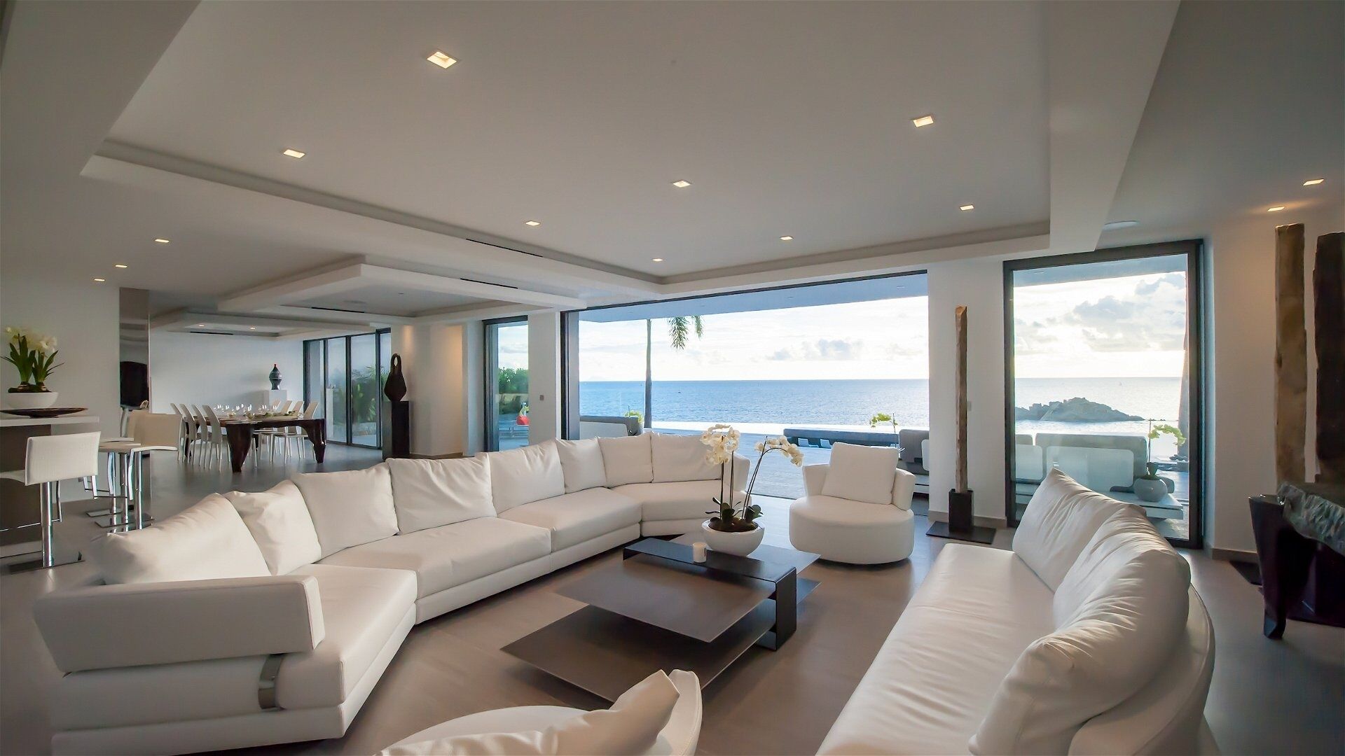 Un salon moderne avec un grand canapé d’angle blanc, une table basse et un coin repas comprenant une table et des chaises.