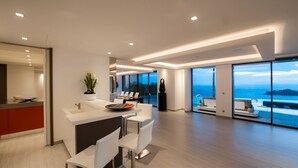 Eine moderne Küche mit einer großen Kochinsel, einem Essbereich mit weißen Stühlen und Meerblick durch große Fenster.