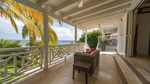 A covered outdoor area with a view of the ocean, a wicker sofa, and a potted plant. - Habitation Saint Louis (3/4 Rooms) (St Barths)