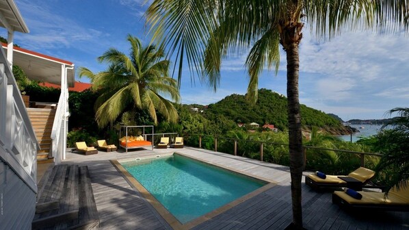 A pool area with a wooden deck, lounge chairs, and a bed with a canopy.