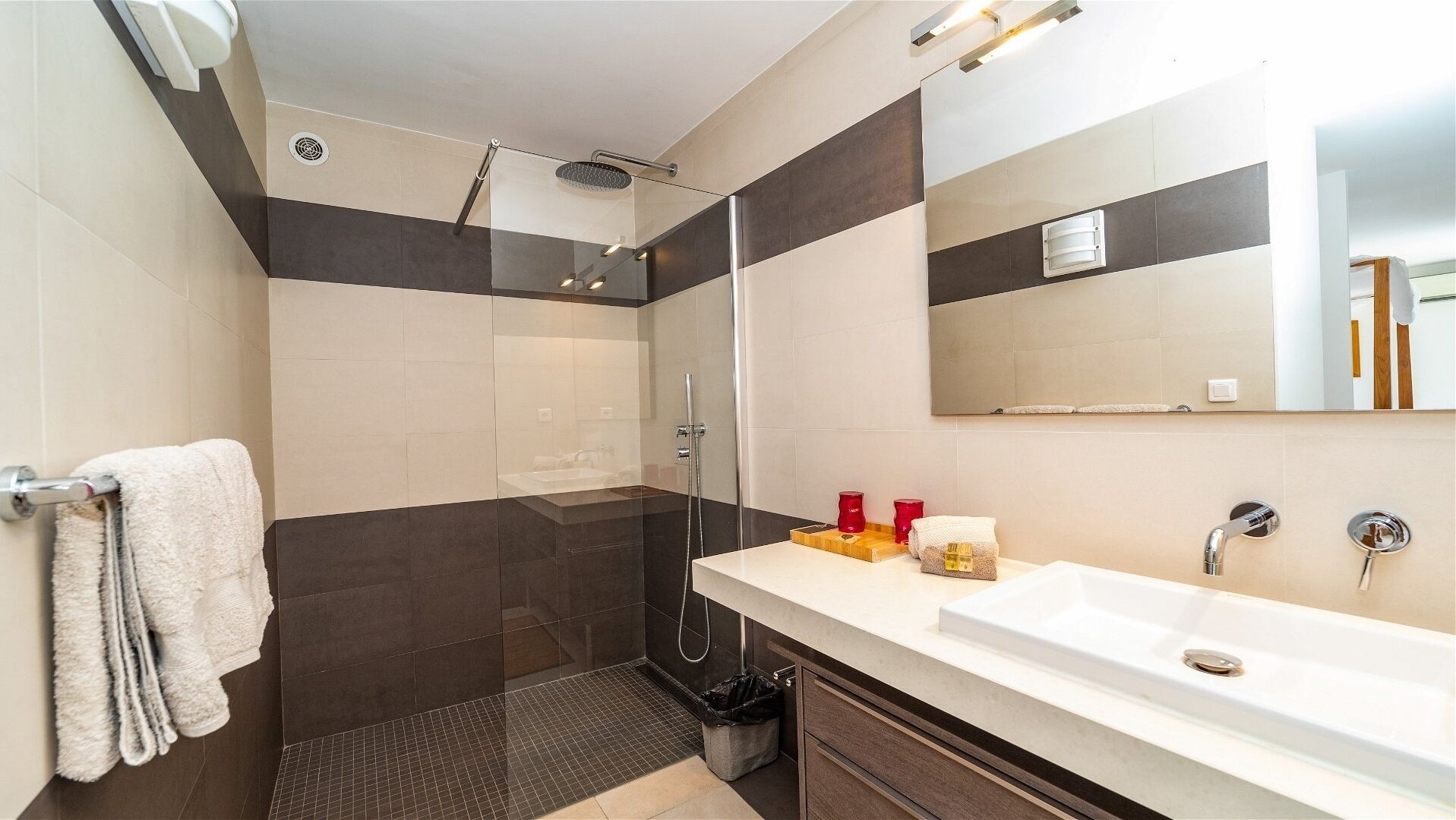 A modern bathroom with a glass-enclosed shower, a large mirror, and a white sink.
