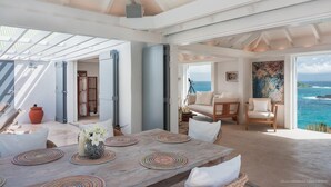 Un vaste espace de vie doté d’une grande table en bois, de sièges confortables et offrant une vue sur l’océan.