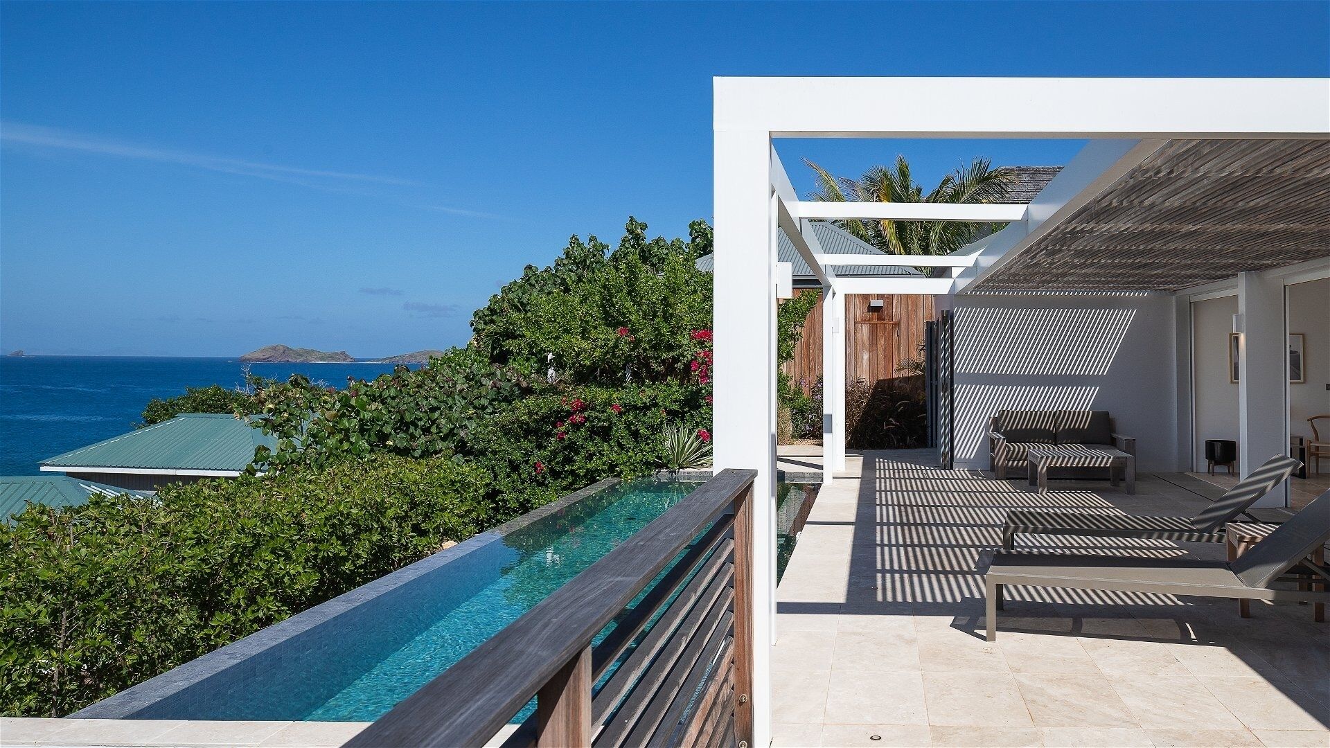 A modern outdoor pool area with a view of the ocean, a wooden deck, and a lounge area with seating.