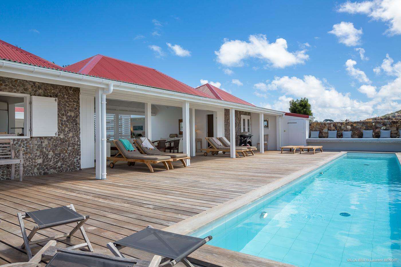 A poolside area with lounge chairs, a covered seating area, and a stone wall.