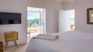 A bedroom with a bed, a television, a wooden dresser, and a balcony with a view of the mountains. - Supersky (2/3 Rooms) Luxury villa (St barts)