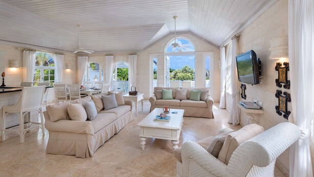 A spacious living room with a high ceiling, white furniture, and a television mounted on the wall.