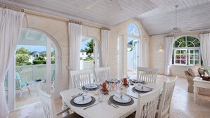 A dining area with a white table set for four, white chairs, and a ceiling fan.