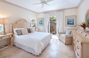 A bedroom with a large bed, a ceiling fan, a desk with a lamp, a chair, a dresser, and two framed pictures on the wall.