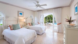 A hotel room with two beds, a ceiling fan, a desk with a lamp, a view of the outdoors, and a decorative plant.