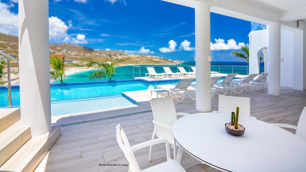 Ein Poolbereich mit Meerblick, weiße Liegestühle und ein Tisch mit einem Kaktus.