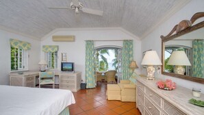 Un dormitorio con cama, televisión, cómoda, silla y vistas al exterior.