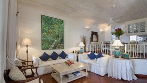 Una sala de estar con un sofá blanco, una mesita de centro y un cuadro de una escena tropical.