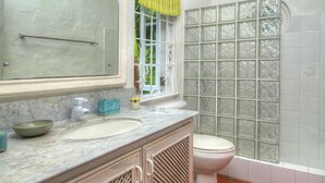 Un baño con lavamanos de mármol, un espejo grande, un inodoro y una ventana con cortina verde.