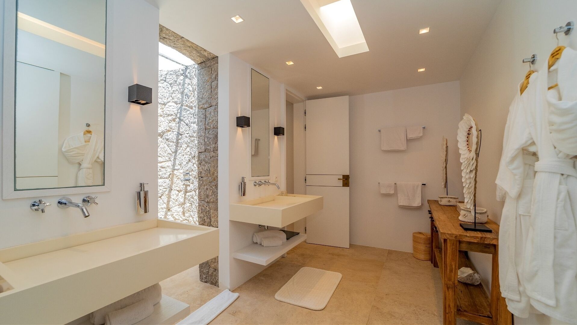 Ein modernes Badezimmer mit zwei Waschbecken, einem großen Spiegel und einer Wand mit Steinverkleidung.