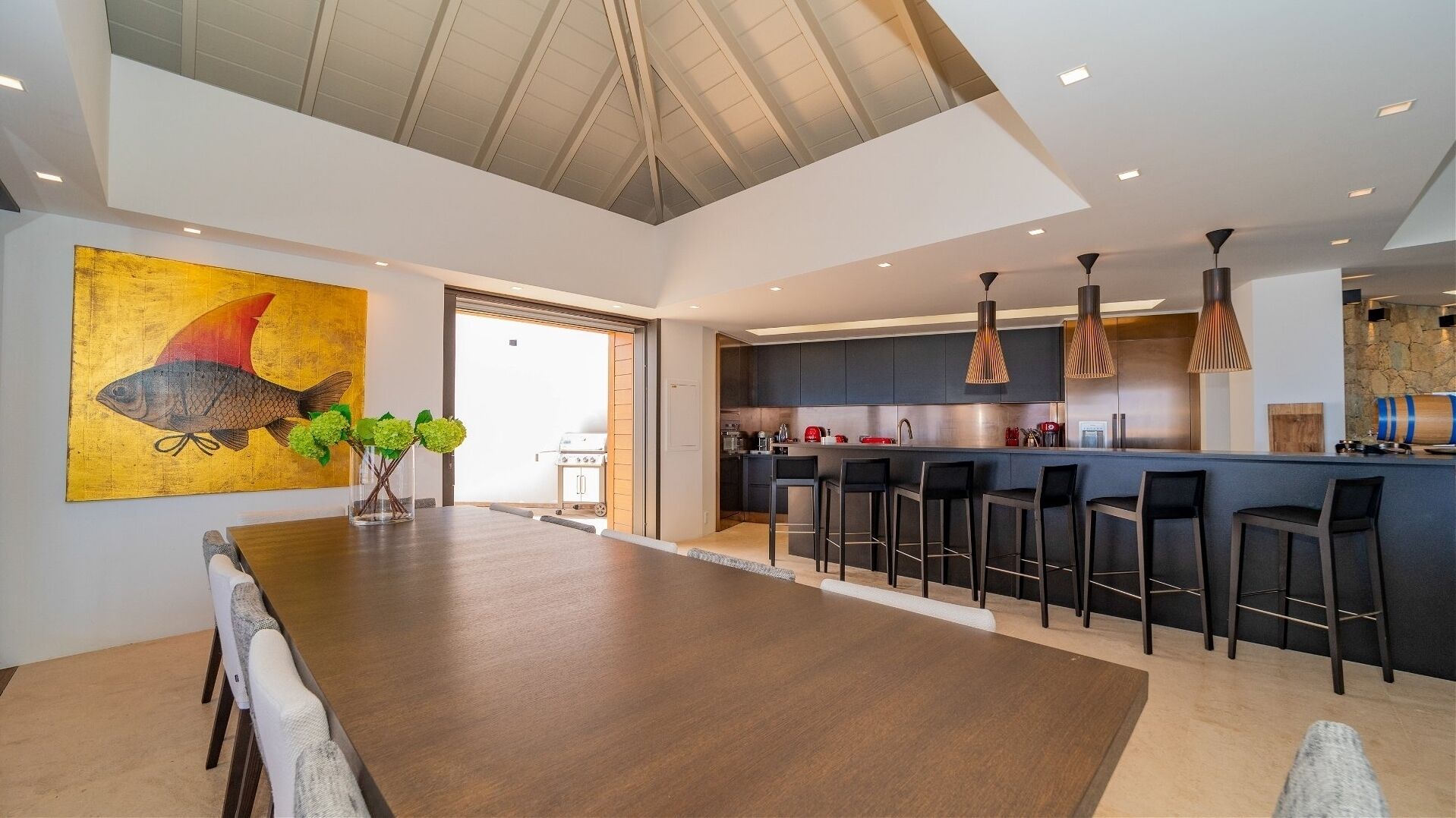 Een moderne keuken met donkere kasten, een centraal eiland met barstoelen en hangende lampen.