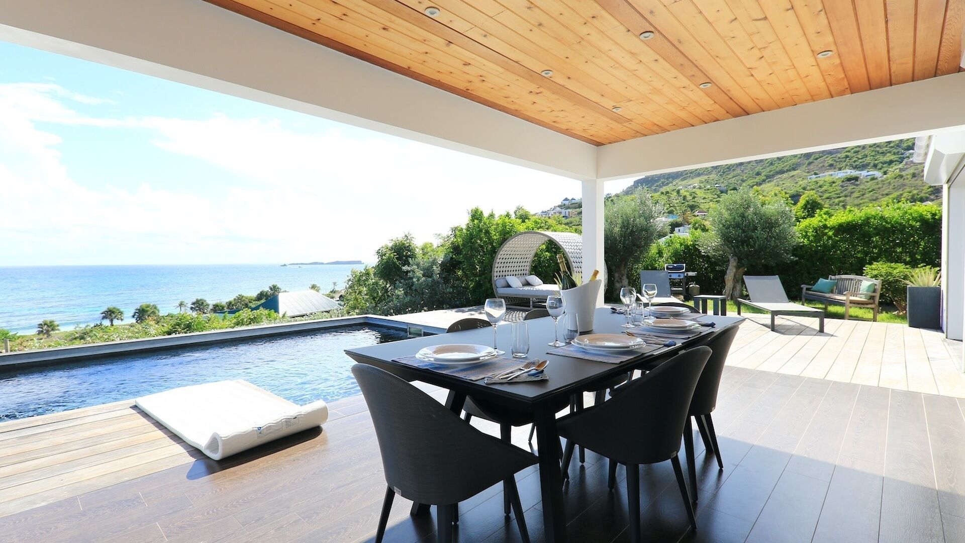 A dining area with a view of the sea, a pool, and a wooden deck.