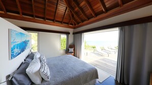 Ein Schlafzimmer mit einem großen Bett, einem Gemälde und Meerblick durch eine Schiebetür.