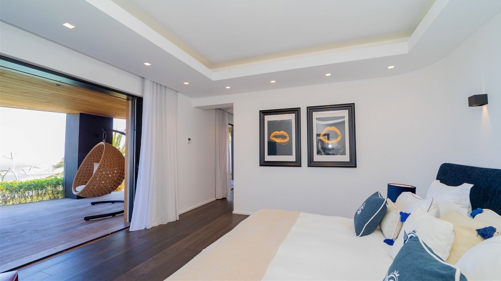 Un dormitorio moderno con una cama grande, una silla colgante y dos obras de arte enmarcadas en la pared.
