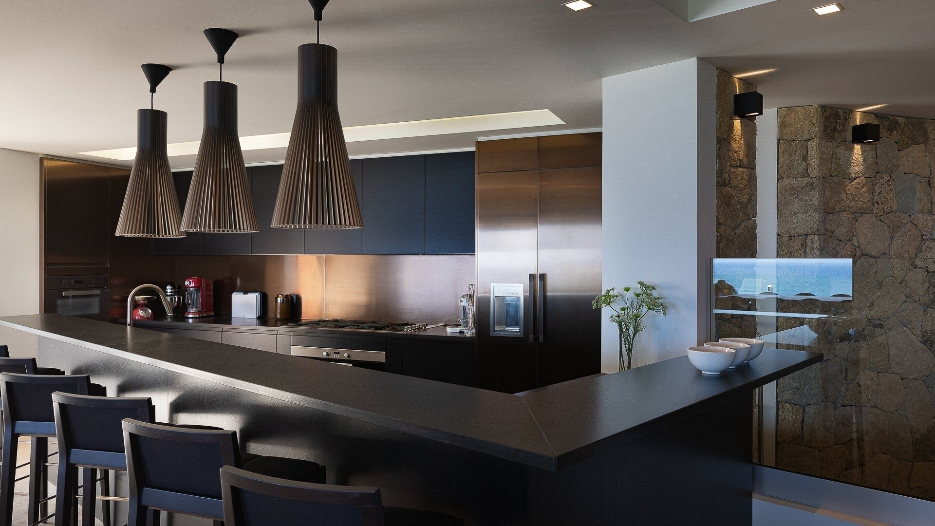 Une cuisine moderne dotée d’un îlot central, d’appareils électroménagers en acier inoxydable et de luminaires suspendus.