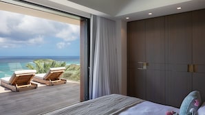 Un dormitorio con una cama grande, un armario y un balcón con dos sillas con vistas al océano.
