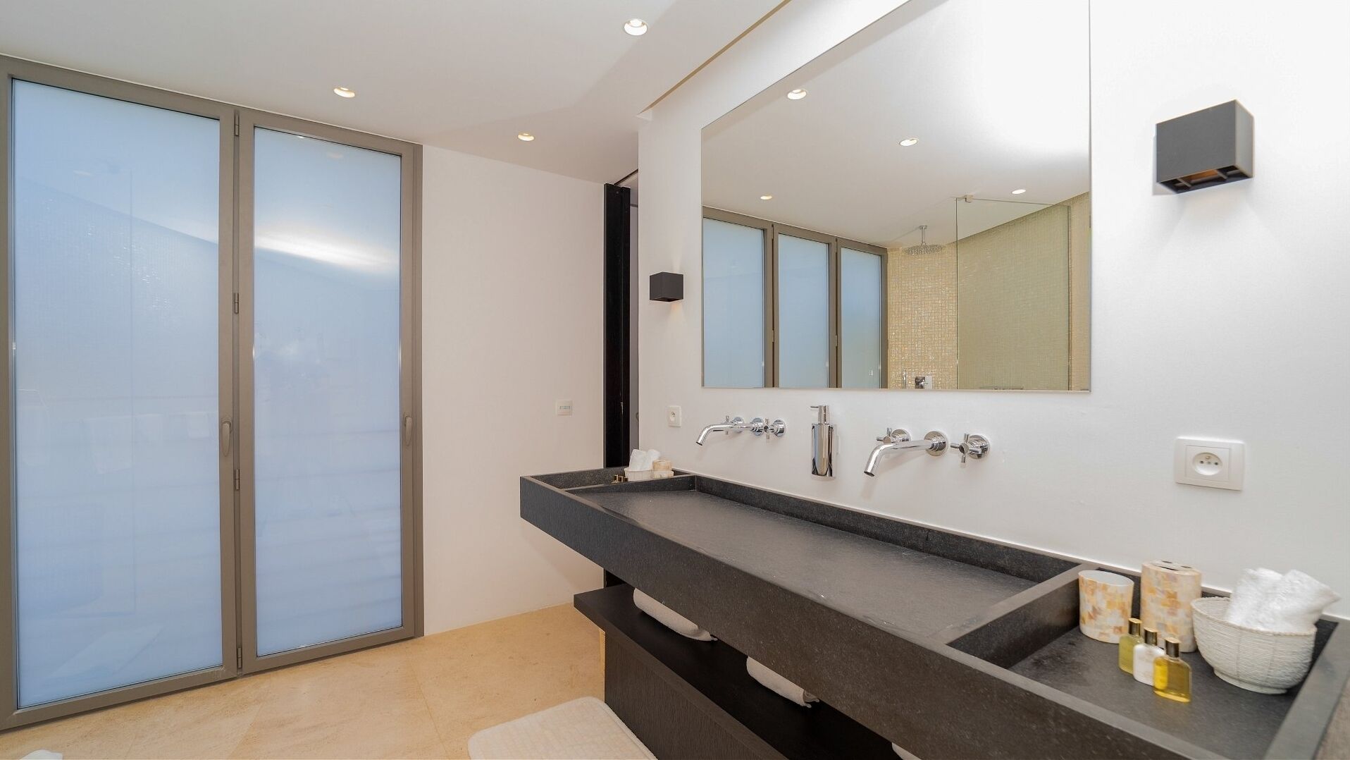 A modern bathroom with a large mirror, a dark countertop, and a glass shower enclosure.
