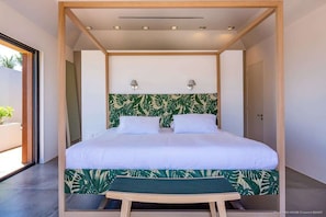 A modern bedroom with a bed, two wall-mounted lamps, and a view of the outdoors. - Eden House (1/3 Rooms) (Marigot)