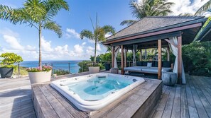 A wooden deck with a hot tub, a covered seating area, and a view of the ocean.