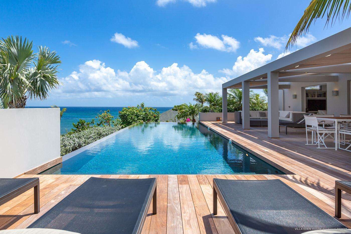 Ein moderner Infinity-Pool mit Holzterrasse, Liegestühlen und Meerblick.