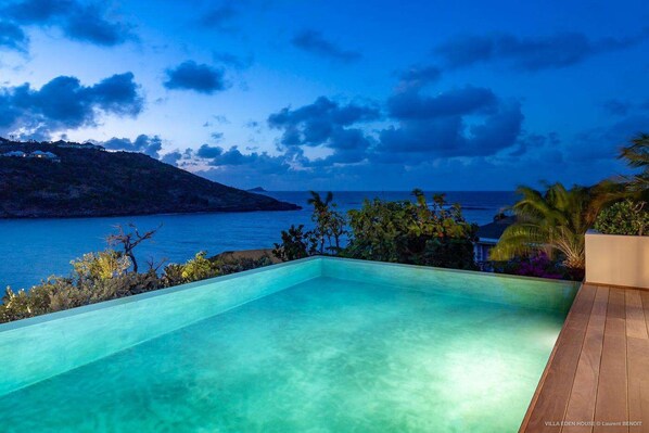 Une piscine à débordement offrant une vue imprenable sur l’océan et un paysage montagneux en toile de fond.