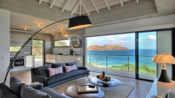 A modern living room with a large sofa, a coffee table, and a view of the ocean. - Eranos (1/2 Rooms) Luxury villa (St. Barts)