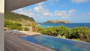 An infinity pool with a wooden deck, lounge chairs, and a view of the ocean and hills. - Eranos (1/2 Rooms) Luxury villa (St. Barts)