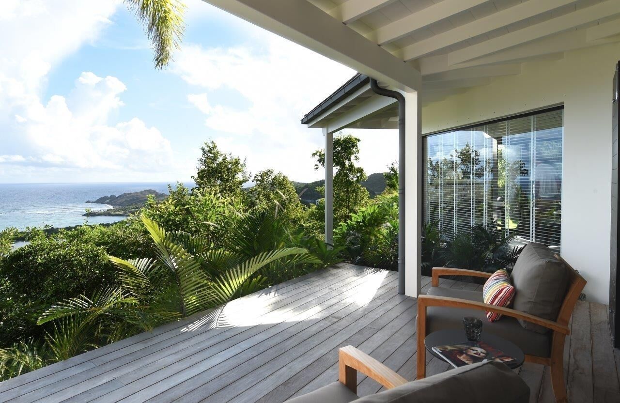 Un balcon avec vue sur l’océan, un plancher en bois et un coin salon avec des coussins.