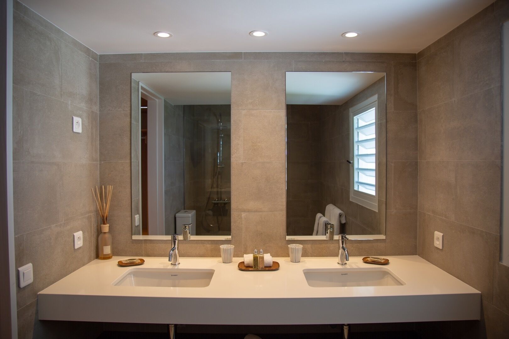 A modern bathroom with two sinks, a large mirror, and a shower visible in the reflection.